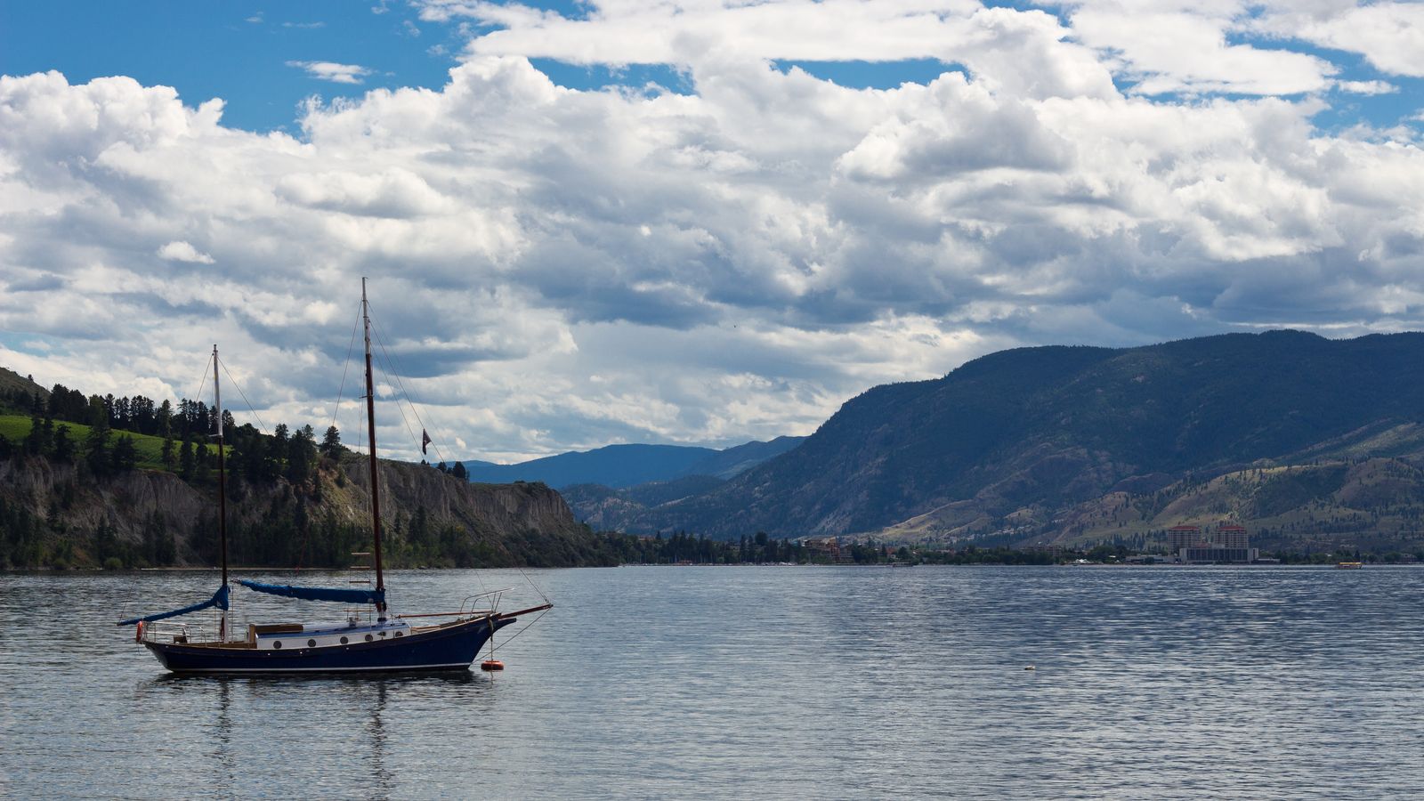 Sailboat drifting on Okanagan Lake at sunset with mountains framing the Kelowna shoreline